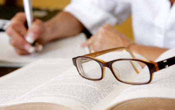 a woman's hand writing notes with eyeglasses on the book
