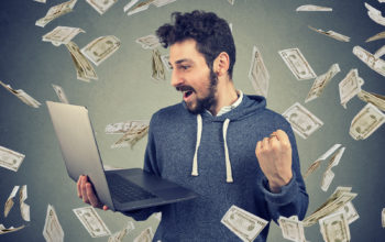 Successful young man using laptop building online business making money dollar bills cash falling down. Money rain. Beginner IT entrepreneur success economy concept